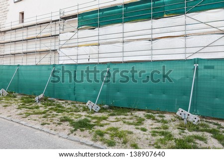 Wall in scaffolding with green protective cloth on reconstruction site