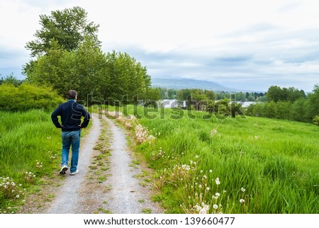 Single adult man walking down the path in the middle of the field near the lake on an overcast day, relaxing