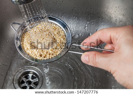 Man holding small strainer with raw quinoa seeds and rinsing it in cold water in the kitchen sink