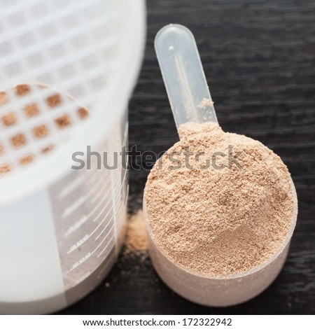 Scope Of Chocolate Whey Isolate Protein Next To The Translucent Protein Shaker, With Focus On The Protein Inside The Scoop