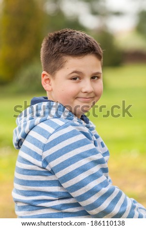 Portrait of a seven years old smiling caucasian boy in the shirt with the blue and white stripes, image taken in the park