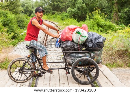 ZAGREB, CROATIA - JUNE 24, 2011: Gypsy boy riding on a bicycle cart carrying bags with plastic bottles and garbage over the train tracks. Gypsy community in Croatia is notorious for scrap collection.