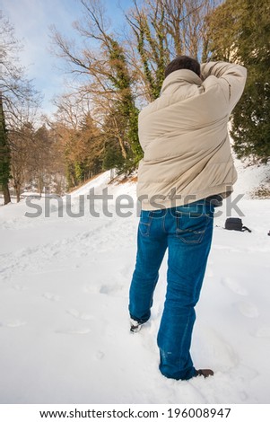 Casually dressed photographer taking pictures of a snow covered scenery on a clear sunny day with blue sky, striking a typical photographer\'s pose
