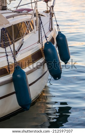 Side of a yacht with three blue fenders, used to protect the boat from hiting the pier or another boat