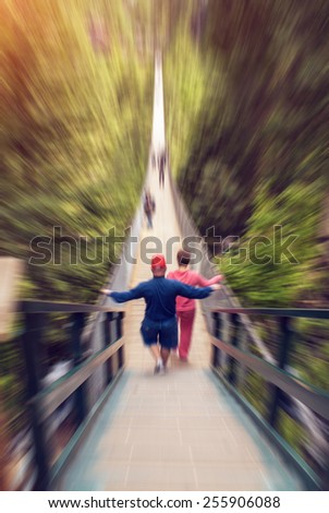 Middle aged couple walking on suspension bridge with their back turned towards camera. Radial zoom effect defocusing filter applied, with vintage instagram look.