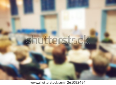 Group of adults attentively listening to the teacher during lectures in the hall. Blurred in post processing; abstract background.