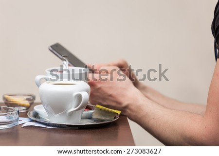 Man texting on his cell phone with a cup of tea on the table in front of him