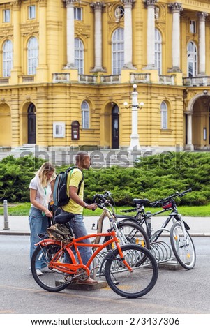 ZAGREB, CROATIA - APRIL 26, 2015: Young mixed race couple standing by the parked bicycles in Zagreb city center, in front of Croatian National Theater, preparing to ride their bikes.