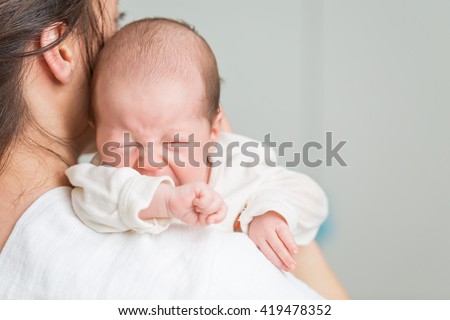 Newborn baby screaming in pain with colic on mother\'s shoulders