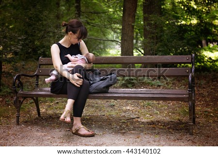 Mother breastfeeding her newborn baby girl in the park on demand, sitting on the bench under the trees, instagram style effect applied
