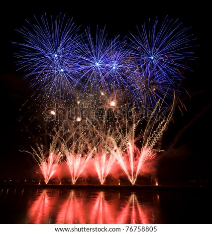 Huge colorful fireworks display with orange, blue and red streaks on the river bank