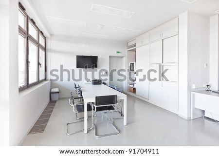 Modern office with white furniture, cupboard, conference desk and walls and with plasma TV on the wall