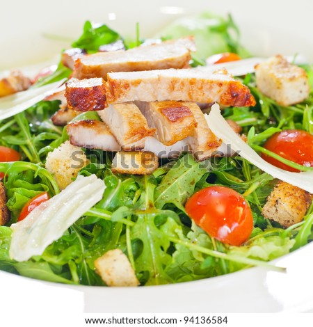 Chicken salad with tomatoes, arugula and bread croutons in the white bowl