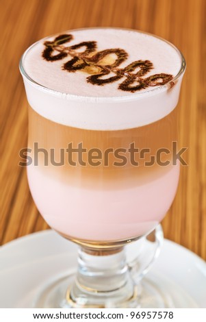 Chocolate decoration on the glass of latte macchiato coffee with grenadine syrup, arranged in layers of coffee and milk with grenadine, on a white plate