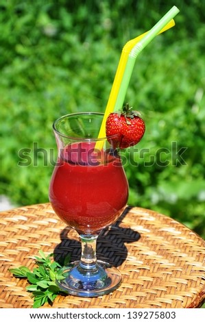 Strawberry smoothie. A glass is on rattan table.