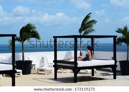 Young woman sitting down on a tanning bed looking into the ocean