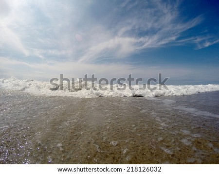 Ocean surf coming towards the camera under a beautiful blue sky and white clouds