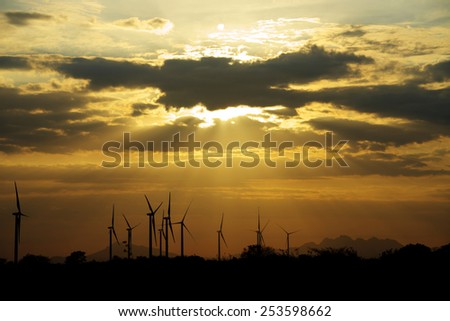 Wind turbines as silhouettes against a beautiful sunset with sun beams shining down
