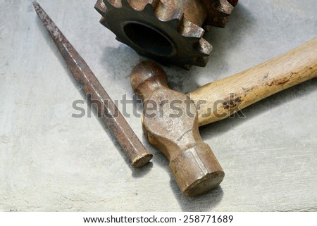 Close up shot of an old rusty ball peen hammer, chisel  and metal part over a concrete surface with natural light