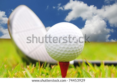 Golf  ball on a tee and driver  against a bright blue sky in the background