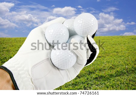 Hand holding several golf balls with a beautiful blue sky and green grass in the background