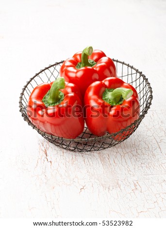 Three fresh picked red bell peppers in wire basket.