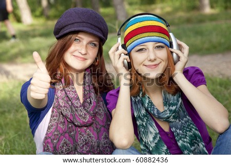 Two smiling happy sisters together in grass outdoors. One with headphones.
