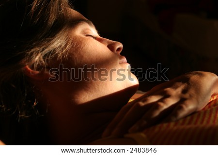 Young woman face over a pillow while sleeping with a ray of light falling on her face. Warm yellow and orange colors dominates the scene.