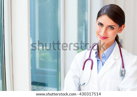 Portrait of smiling female doctor with stethoscope around neck. Confident medical professional is wearing lab coat. She is standing in clinic.