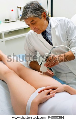 caucasian woman receiving laser treatment at the leg from a male doctor