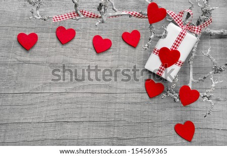 Gift box wrapped in paper with a red checkered ribbon and many red hearts on a wooden background for mother\'s day, birthday or valentine\'s day