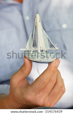 Man holding a small toy sailing boat - concept for sailing or cruising