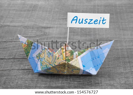 Paper boat folded out of a map with a time-out sign on an grey wooden background