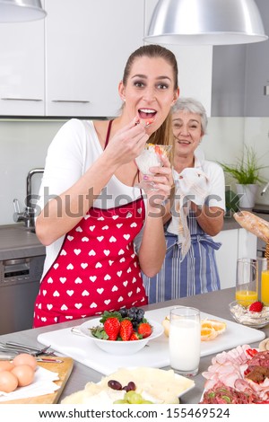 Young woman cooking and eating with her mother  in the kitchen