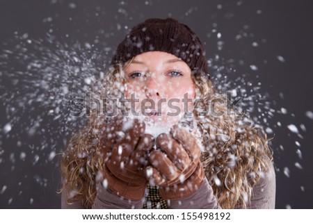 Young woman in winter clothes blowing snowflakes from her hand