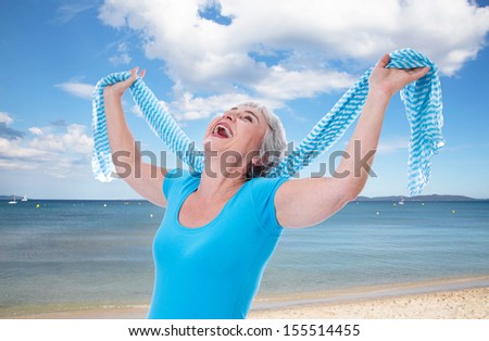 Happy senior woman stretching her hands up on holidays. At the beach in summer times.