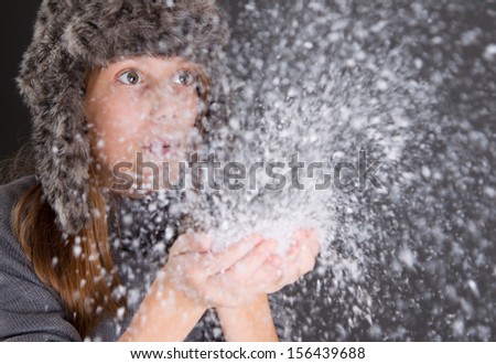 Young brunette woman in flaphat blowing snow.