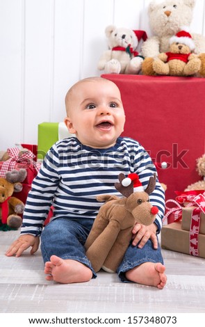 First Christmas: barefoot baby with moose amongst presents and cuddly toys