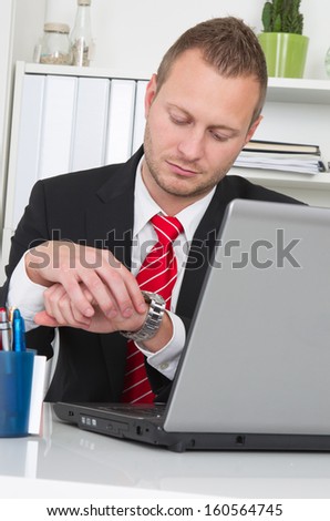 Businessman looking at watch with laptop - end of work