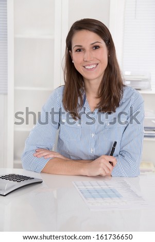 Successful business: woman smiling in blue blouse sitting at desk with folded arms