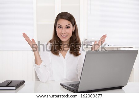 Dream job: successful smiling businesswoman sitting at desk with laptop and arms up