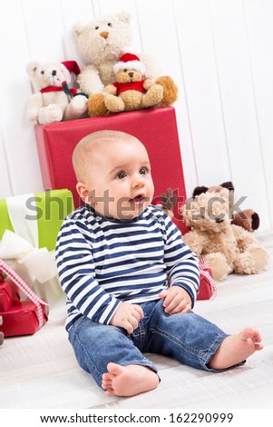 Christmas and birthday - cute baby sitting barefoot and looking excited surrounded by teddy bears and presents