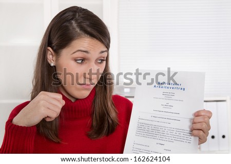 Young disappointed woman staring at business contract in german language - time work