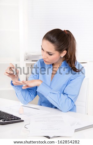 Businesswoman in a blue blouse is making her nails in the office - during lunch time.