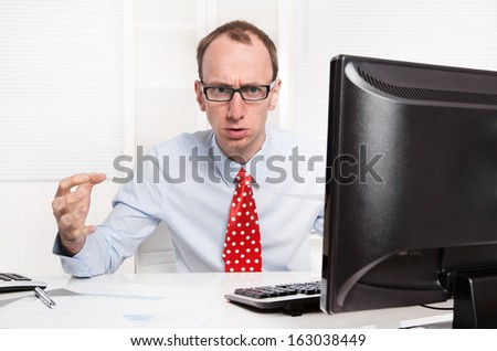 Businessman with bald and glasses aggressive and in rage sitting at his office with computer.