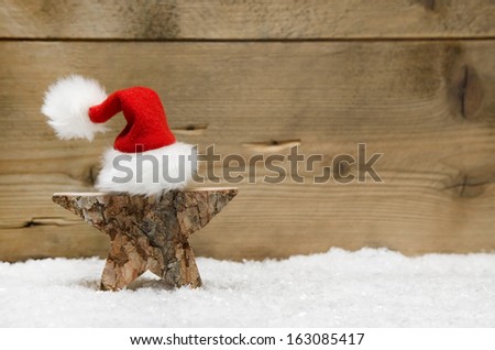 Wooden star with red santa hat on wooden background - handmade idea for a greeting card