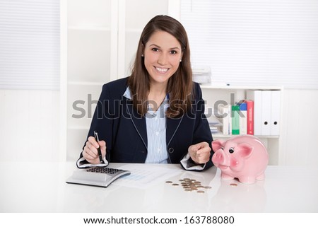 Smiling pretty caucasian businesswoman with piggy bank at office.