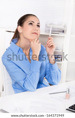 Young woman in blue blouse sitting at desk and dreaming