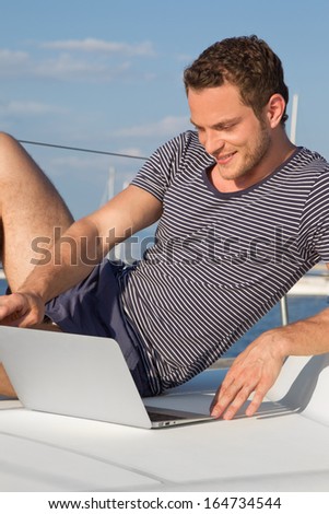 Businessman is working with laptop during vacation on a sailboat - sail trip.