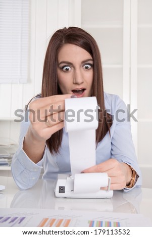 Young shocked accountant with open mouth looking at calculating machine.